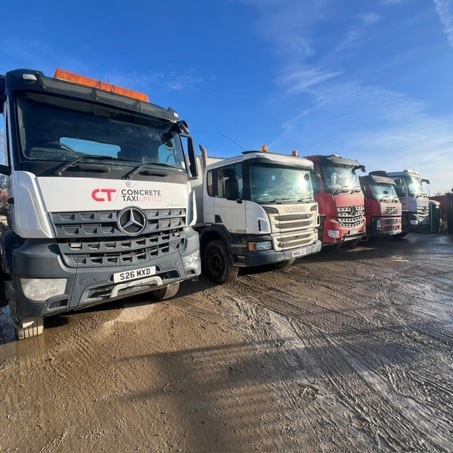 Row of commercial concrete delivery trucks parked in a yard on a sunny day